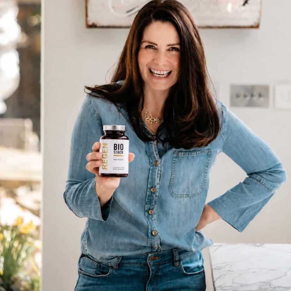 A woman holding a bottle of NAD Regen in her kitchen
